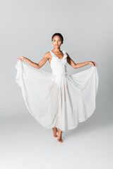 Fototapeta na wymiar barefoot graceful african american ballerina in dress dancing on white background