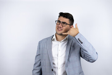 Business young man wearing a casual shirt over white background confused doing phone gesture with hand and fingers like talking on the telephone