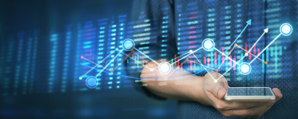 Hand holding smartphone device and touching screen. businessman trader looking on with graphs analysis candle