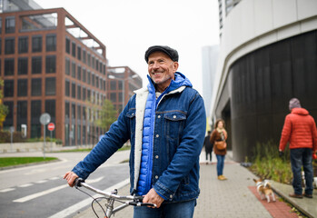 Fototapeta na wymiar Happy senior man with bicycle outdoors on street in city, walking.