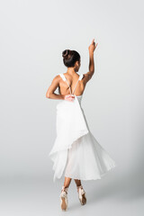 Fototapeta na wymiar Back view of graceful African American ballerina in dress dancing on white background