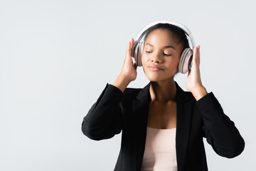 african american businesswoman listening music in headphones isolated on grey