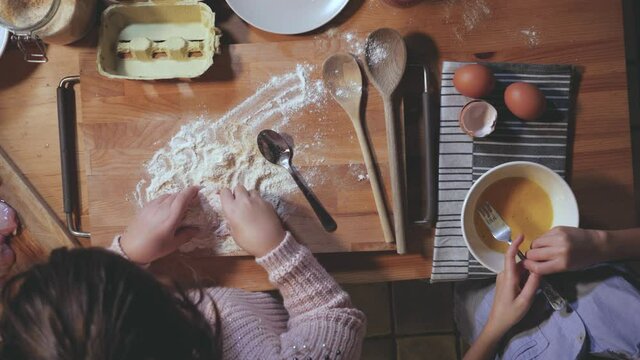 two children sister and brother, cooking at home in the evening. Top view, girl and boy preparing dinner on the table with eggs, flour, wood tablespoons. Happy kids in home kitchen