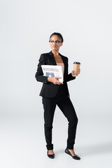 african american businesswoman with business newspaper and coffee to go isolated on grey