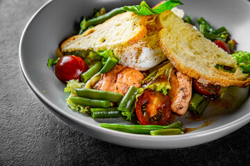 Green Bean Salad with Boiled Eggs, Salmon, Tomatoes and Arugula in a bowl on Dark grey black slate background