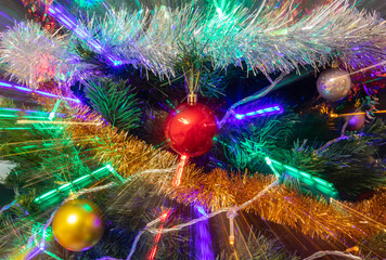 Decorated Christmas tree closeup shot. Red and golden balls, illuminated garland with red, blue, orange, green lights. New Years, winter holiday light decoration with light trails. Long exposure