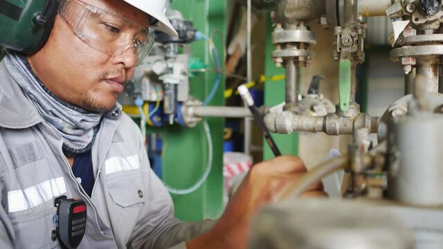 An employee holding a clipboard examining something in an industrial plant and recording the results on a paper sheet.