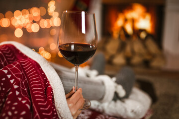 Woman drinking wine from glass sitting and relaxation near fireplace and christmas tree.
