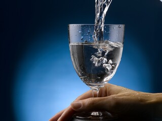 Wet hand is holding a stem glass of water.