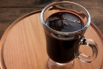 Dark hot chocolate in a glass cup on wooden table. Top view. Hot winter drink on wood background