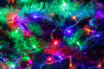 Obraz na płótnie Canvas Decorated Christmas tree closeup shot. Red and golden balls, illuminated garland with red, blue, orange, green lights. New Years, winter holiday light decoration. Long exposure