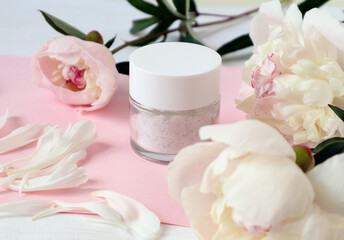 Obraz na płótnie Canvas Body care cream among pastel peonies, close-up, side view - the concept of pleasant self-care