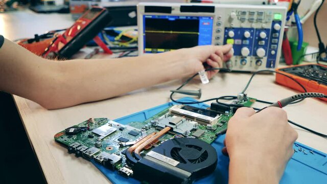 Worker testing laptop motherboard using oscilloscope