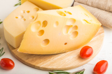 Various types of cheese with rosemary and tomatoes on wooden board on a white wooden background. Side view, close up.