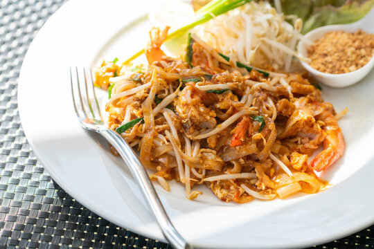 Pad Thai or Thai traditional stir-fried noodle with shrimps on white plate, close up juicy Pad Thai on white dish with fork, beautiful food decoration, natural light image.