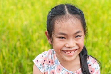Beautiful portrait of Asian child girl on vacation, cute face with big smile, black long hair, close up cut face, blurred background rice field. Space for copy and design.