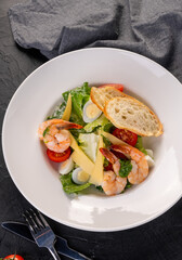 salad with tiger shrimps(prawns) in a white plate on a dark background. Caesar Salad with seafood. Top view. Copyspace