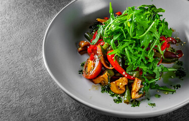 Vegetarian vegetable salad with mushrooms, arugula, tomato, beans and pepper in a bowl on Dark grey black slate background