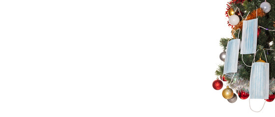 Christmas tree decorated with face masks, colorful balls, and tinsel. Celebrating holidays during pandemic. Safe holiday celebration concept. Isolated on white background. Banner size, copy space