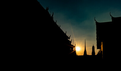 Naklejka premium Silhouette Buddhist temple, sunset sky, sun with light beam, low light image. Beautiful sunset scene from Wat Pho or Wat Phra Chetuphon, famous Buddhist temple of Thailand. Blank space for copy.