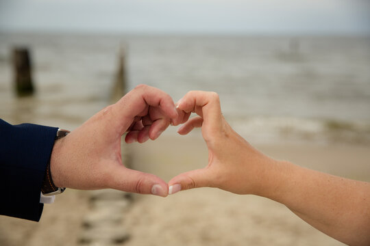 Paar formt Herz mit Fingern an der Ostsee