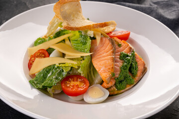salad with salmon slices in a white plate on a dark background. Caesar salad with seafood