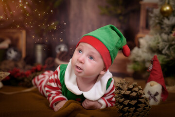 Happy baby elf helper of Santa in costume Santa Claus with gift at christmas tree