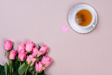 Bouquet of pink roses, cup of tea and pink heart on pink backround.