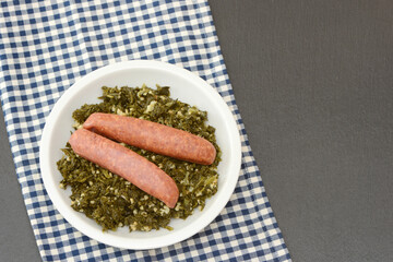 Fresh cooked kale with sausages in the pan on black background