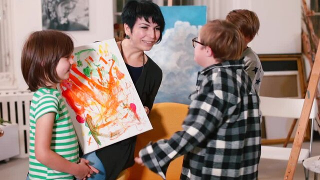 An art school student with Down syndrome explains to the teacher and other students without disabilities the meaning of his abstract painting in orange colors. Embracing inclusion, team positive mood.