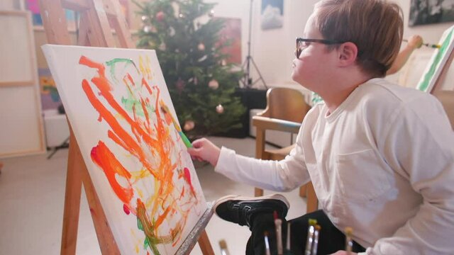 Toothbrush as a painting tool. A boy with Down syndrome paints on canvas in a studio, provide arts and education opportunities for people with disabilities and increase access to the arts for all. 
