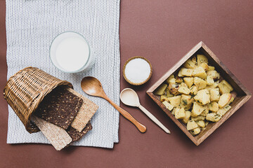 Delicious potatoes fried with dill on a wooden plate, salt, various breads and milk. Table top view. Country lunch.