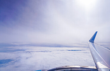 Wing of an airplane flying above the morning clouds. Looking through window aircraft during flight in wing