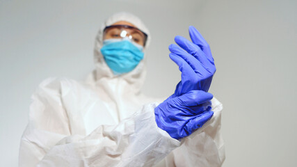 Medical worker in protective suit puts on gloves.