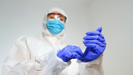 Medical worker in protective suit puts on gloves.