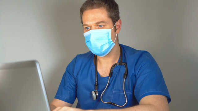 Medical Doctor In Protective Mask Having Video Conference With Patient.