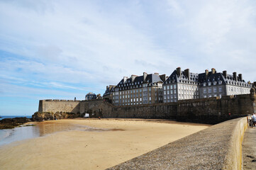 Fototapeta na wymiar View of the buildings of the fortress Saint-Malo, France. Sandy seashore at low tide.
