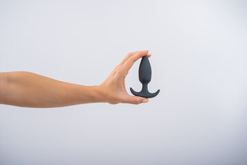 Faceless woman holding a black anal plug on a white background. Assortment of sex shop
