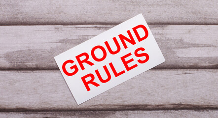 On a wooden background, there is a white card with red text GROUND RULES