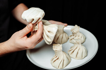 the hand holds the chikali by the tail. Khinkali in a Georgian restaurant in hand. Georgian cuisine