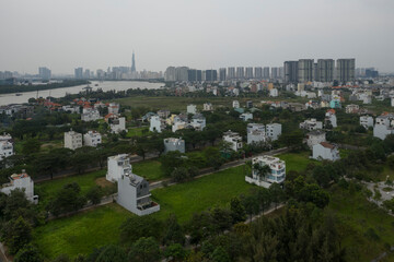 panoramic drone shot of Thu Thiem development area of Ho Chi Minh City with Saigon river, city skyline, villa and high rise buildings and rice fields, Vietnam