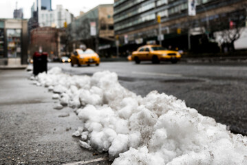 Melting snow in New York City street and sidewalks with defocused yellow taxis in the background