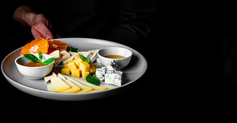 chef in a black suit holds in his hands Cheese plate on Dark grey black background