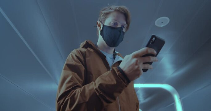 Clean minimalistic shot of futuristic young man in face mask in modern urban environment. Busy city life in subway underground or airport scene, new normal covid times.Use smartphone for contact trace