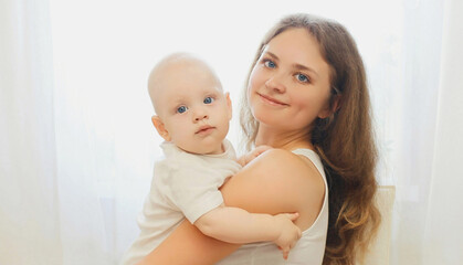 Portrait close up of happy smiling mother with baby over a white window at home
