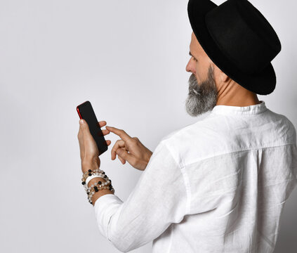 View Over The Shoulder Of A Bearded Man In A Black Hat About To Press A Finger On A Blank Touch Screen Of A Mobile Phone Holding In His Hand On A White Background. Advertising And Banner Concept