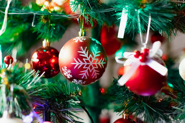 Bright red Christmas toys on the branches of an artificial Christmas tree. Snow balls and berries. A variety of festive accessories shimmer next to colored garlands and lanterns