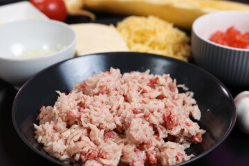 A set of fresh vegetables on a wooden kitchen table for cooking. Onions, garlic, red tomato, yellow zucchini , fresh meat and cheese on the kitchen table.