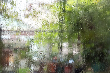 Rain drops pouring on the wet misty window with blurred natural background