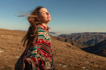 girl in a colored poncho in mountains enjoying the wind. portrait of a beautiful young woman in the mountains